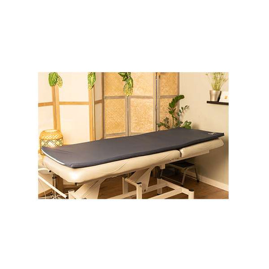 Matelas énergétique bleu conçu pour optimiser les séances de relaxation et de soin, présenté sur une table de massage en bois dans une pièce chaleureuse agrémentée de plantes et d'éléments naturels.